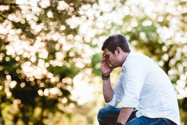 man looking sad in front of some trees in a white shirt
