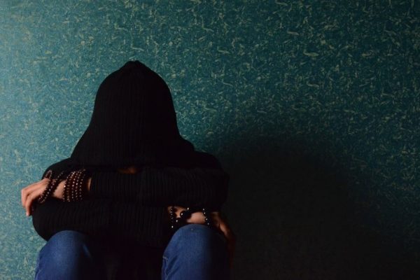 person in black hoodie with hands face in knees