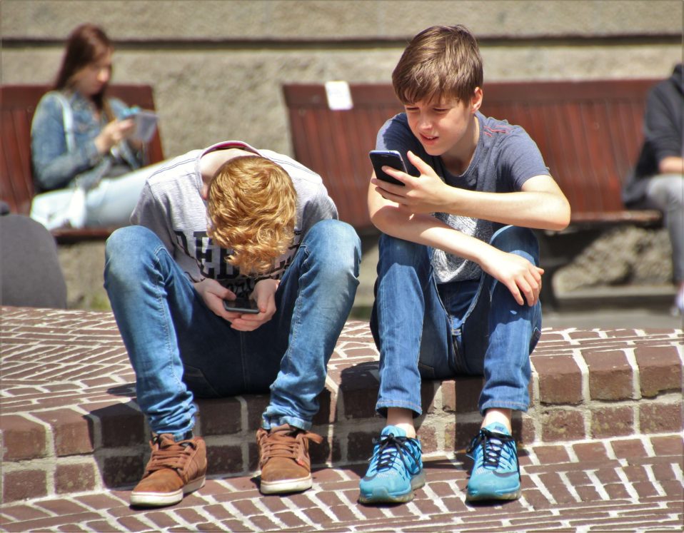 children sitting at side of road safely using social media on their phones